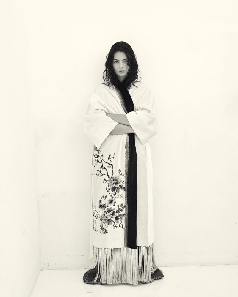 Monochrome portrait of a woman in a patterned robe with arms crossed, set against a white corner background. Beauty and fashion.