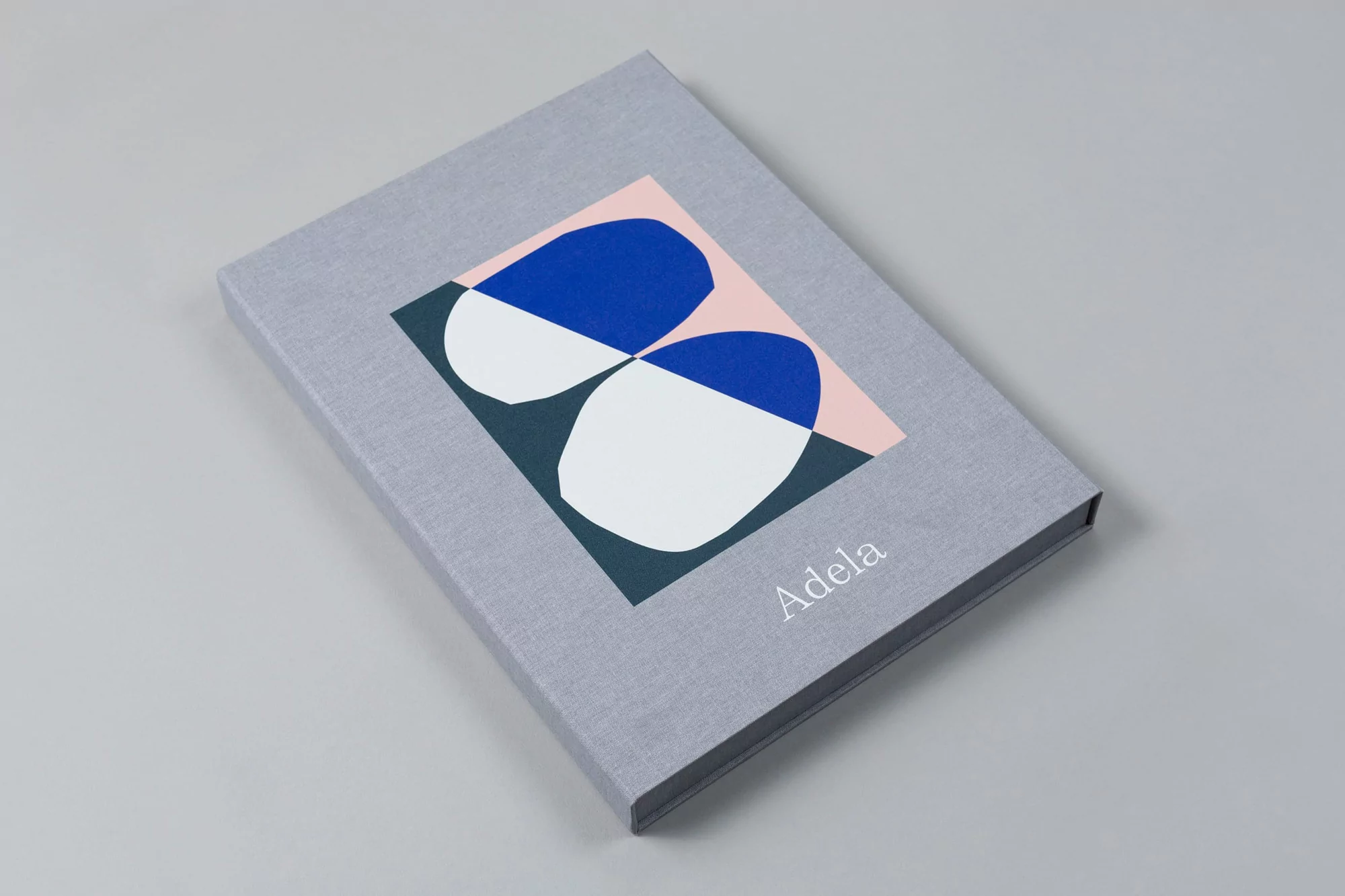 Grey fabric-bound box featuring an abstract geometric print and the Adela brand name on a neutral grey background.
