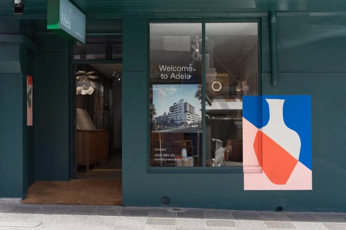Facade of the Adela store front featuring an abstract painting next to the window and an open door leading into the store's interior.