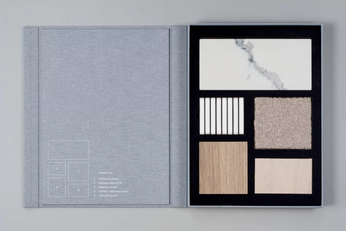 Material sample book with tiles, wood, and carpet swatches arranged in a black frame, offering a variety of textures and colours.