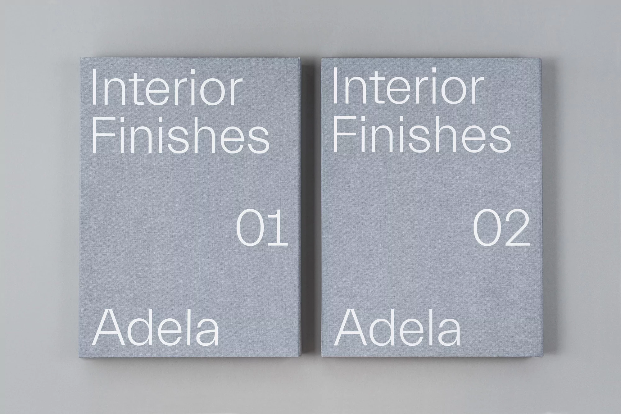 Two gray books titled Interior Finishes, volumes 01 and 02, sit side-by-side on a light gray background in a simple product shot.