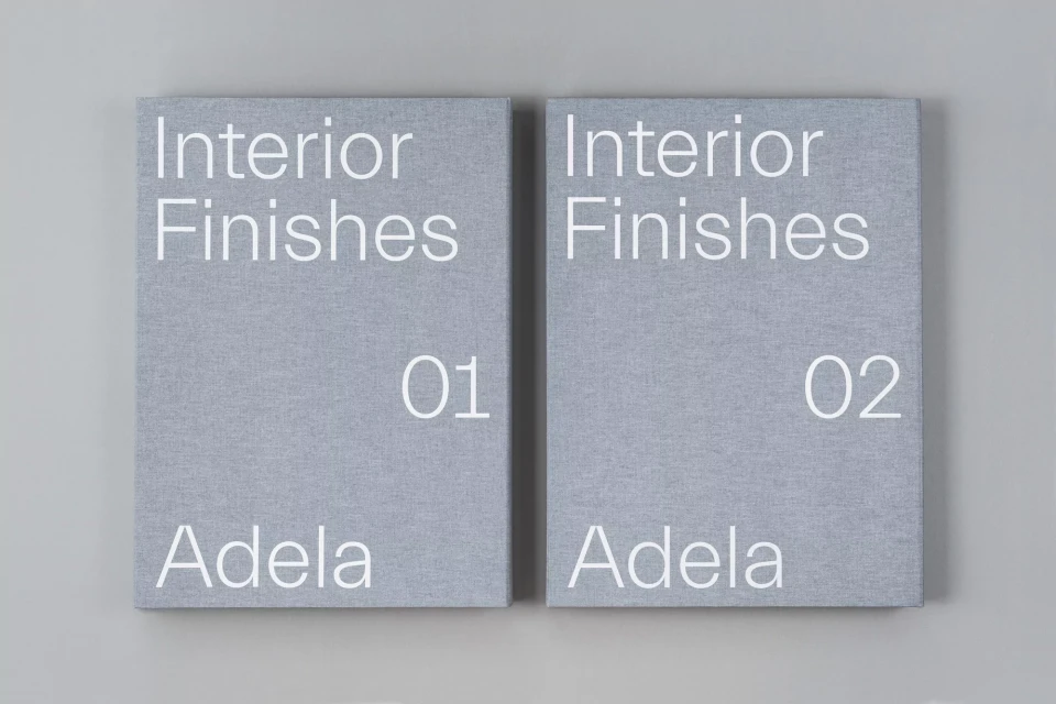 Two gray books titled Interior Finishes, volumes 01 and 02, sit side-by-side on a light gray background in a simple product shot.