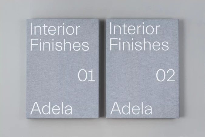 Two gray books titled Interior Finishes, volumes 01 and 02, sit side-by-side on a light gray background in a simple product shot.