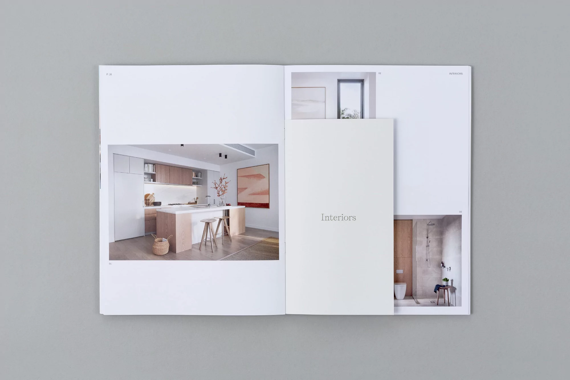 Open magazine displaying interior design photos of a modern kitchen and bathroom in bright, neutral tones on a gray surface.