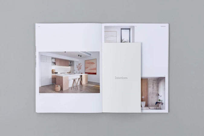 Open magazine displaying interior design photos of a modern kitchen and bathroom in bright, neutral tones on a gray surface.
