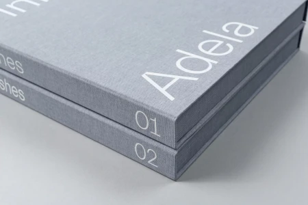Two grey fabric-bound presentation boxes stacked with white typography reading Adela and numbers 01 and 02