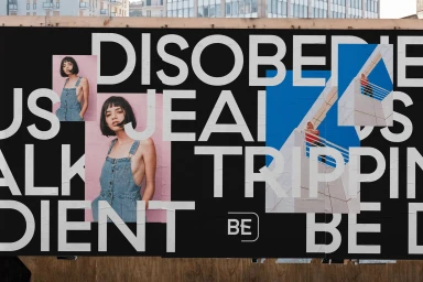 Large outdoor paste-up poster featuring bold typography and layered photography showcasing a brand identity.
