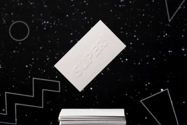 Floating white business card with debossed typography above a stacked pile against a dark starry background