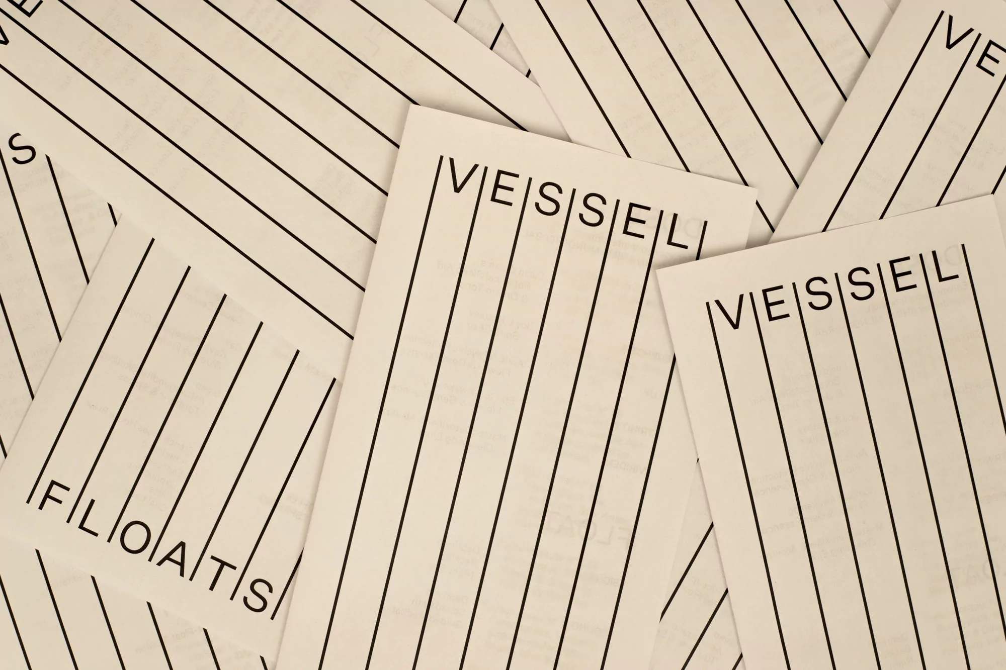 Pile of white paper with black print featuring the words 'vessel' and 'floats' alongside lined guide, creating a structured and textured composition.