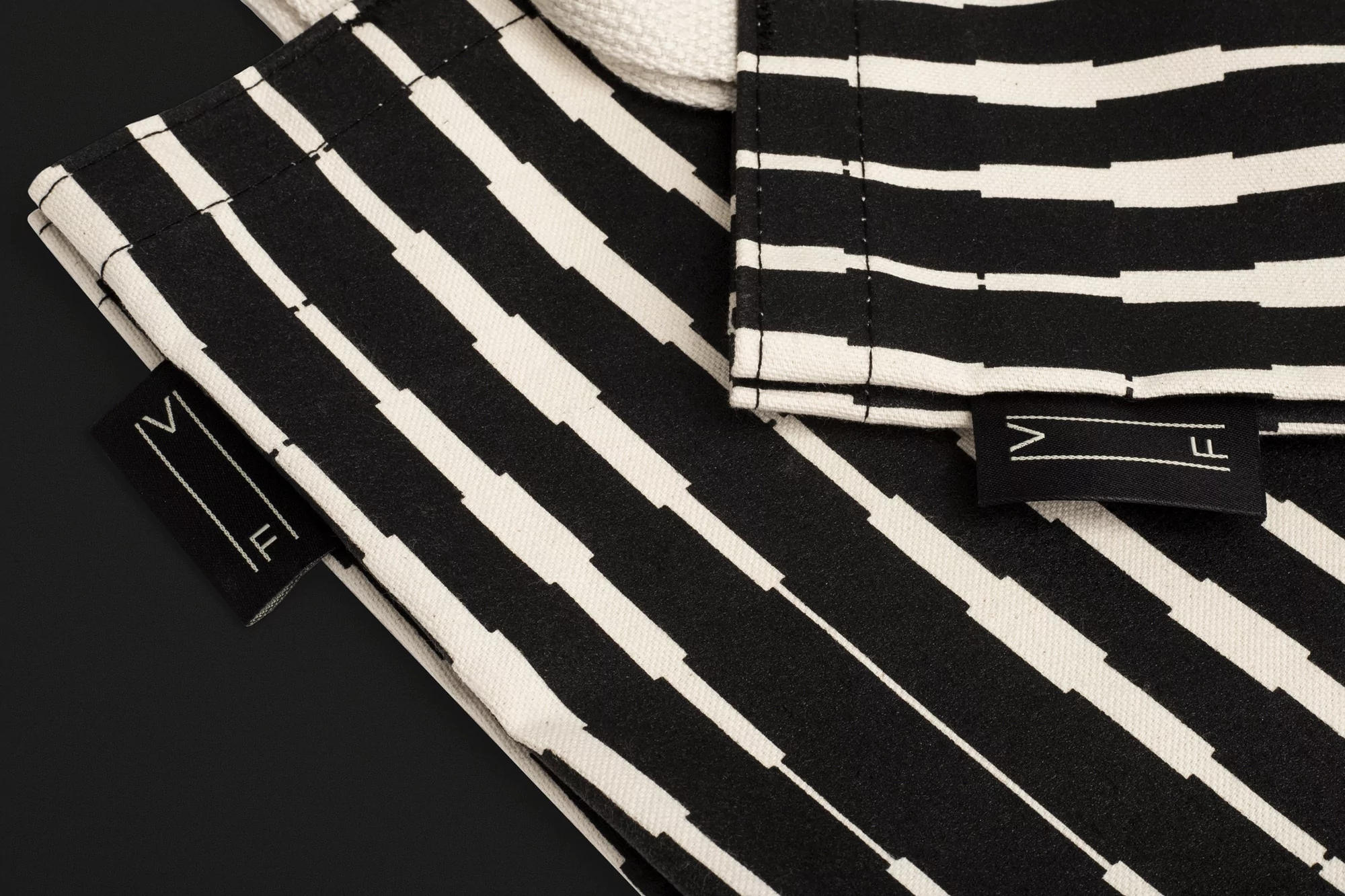 Close-up of two black and white patterned fabric bags with 'VF' logo tags on a black background. Monochrome textile product shot.