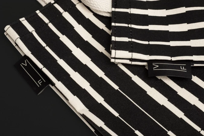 Close-up of two black and white patterned fabric bags with 'VF' logo tags on a black background. Monochrome textile product shot.