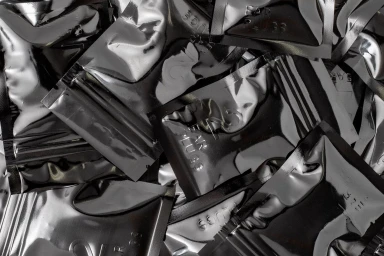 Close-up arrangement of metallic silver foil packets overlapping in a glossy, reflective pile.