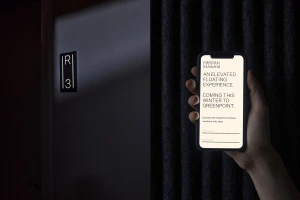 Hand holding a smartphone displaying Vessel Floats brand identity against a dark textured wall and door