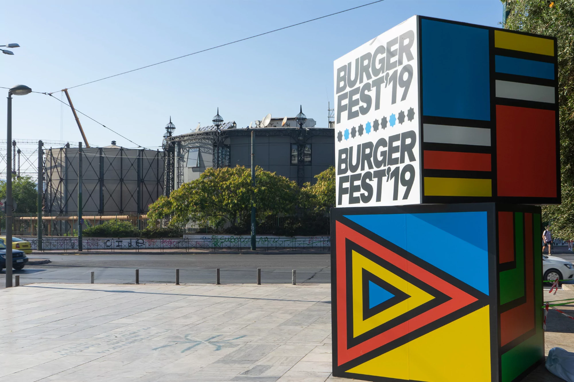 Burger Fest '19 advertisement on a stack of colorfully painted cubes in an outdoor urban setting with industrial buildings.