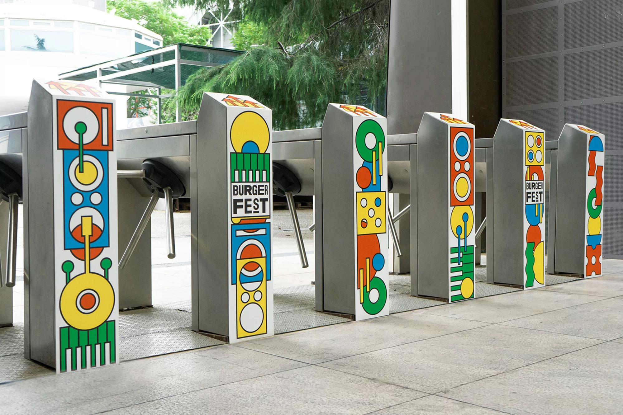 Outdoor shot of turnstiles with colorful geometric designs, featuring 'Burger Fest' signage, in a modern architectural setting with daylight.