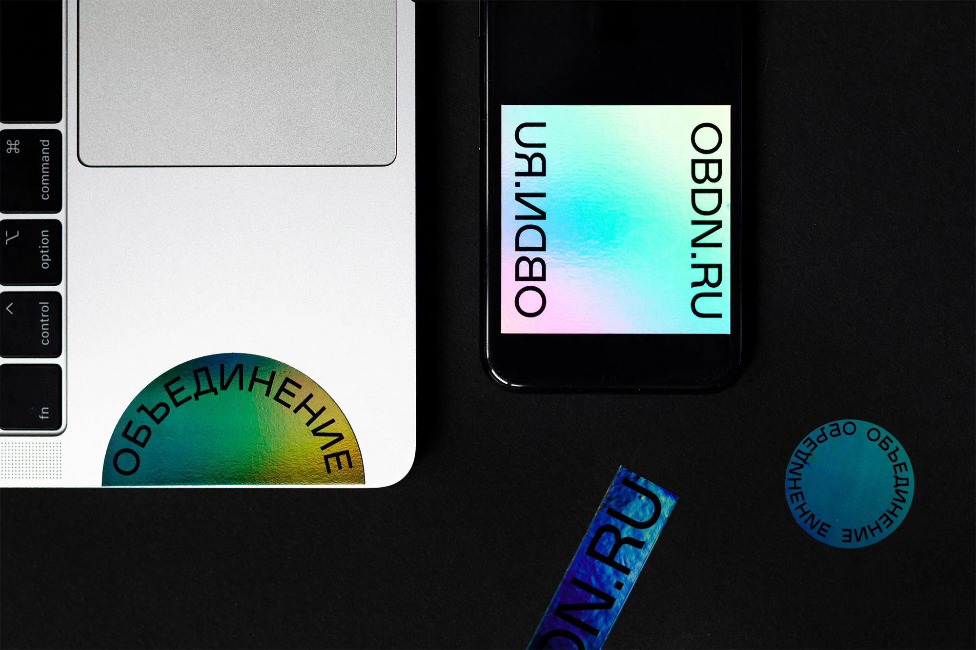Still life featuring a silver laptop, a black smartphone, stickers with Russian text, and a black surface. Flat lay, top-down perspective.