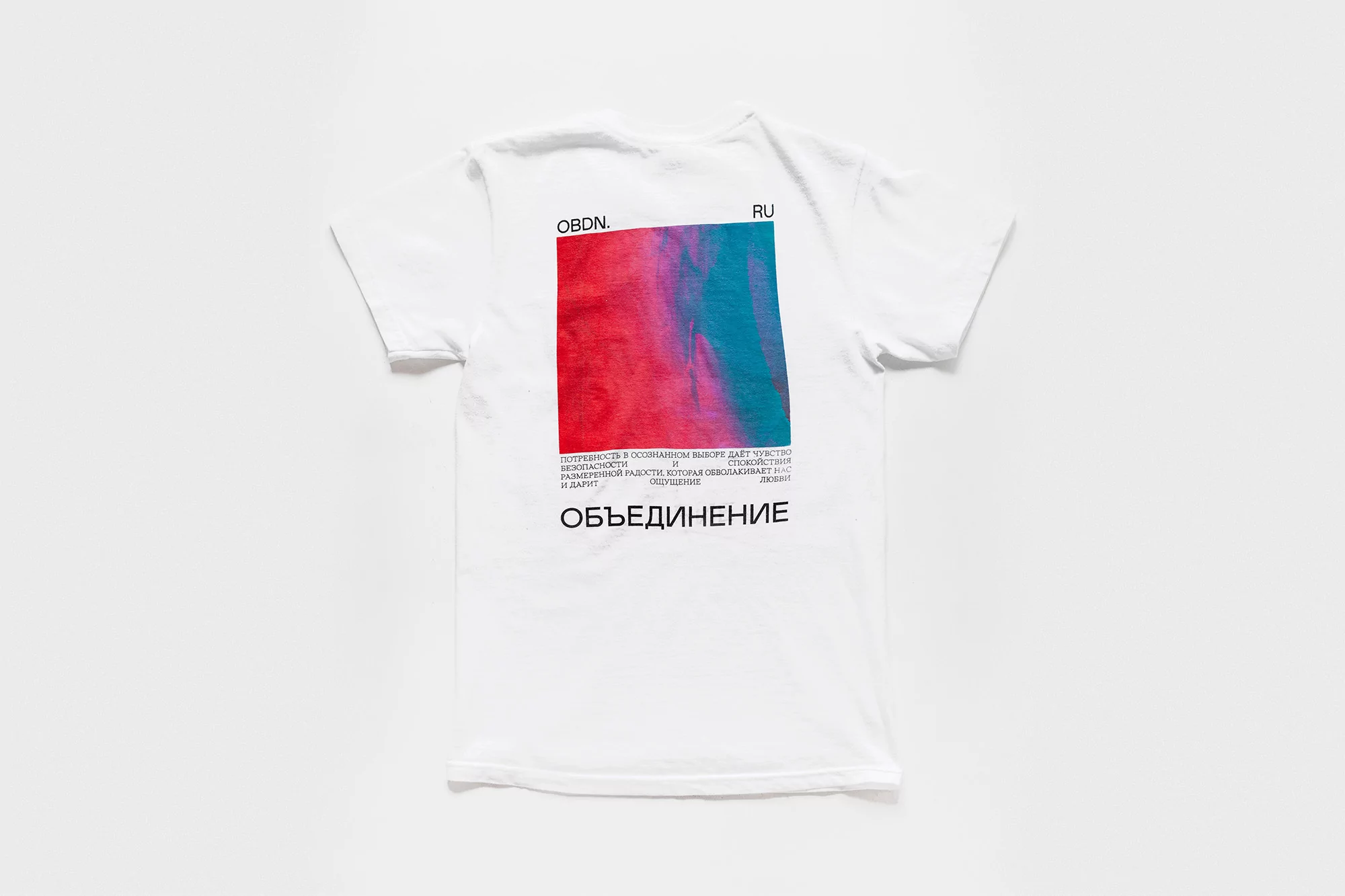 White t-shirt on white backdrop, square graphic in pink and teal with Russian text, simple studio photography for fashion brand.