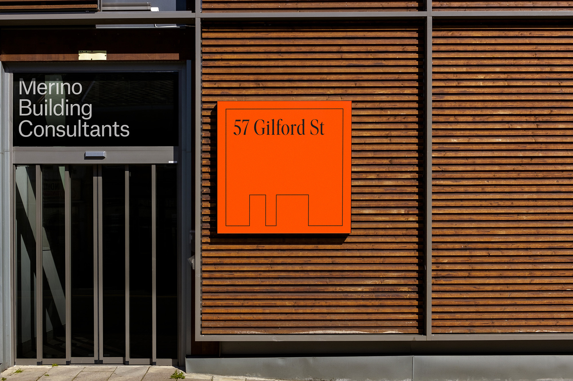 Exterior shot of Merino Building Consultants, featuring a modern facade with wooden panels and a distinctive orange signage.