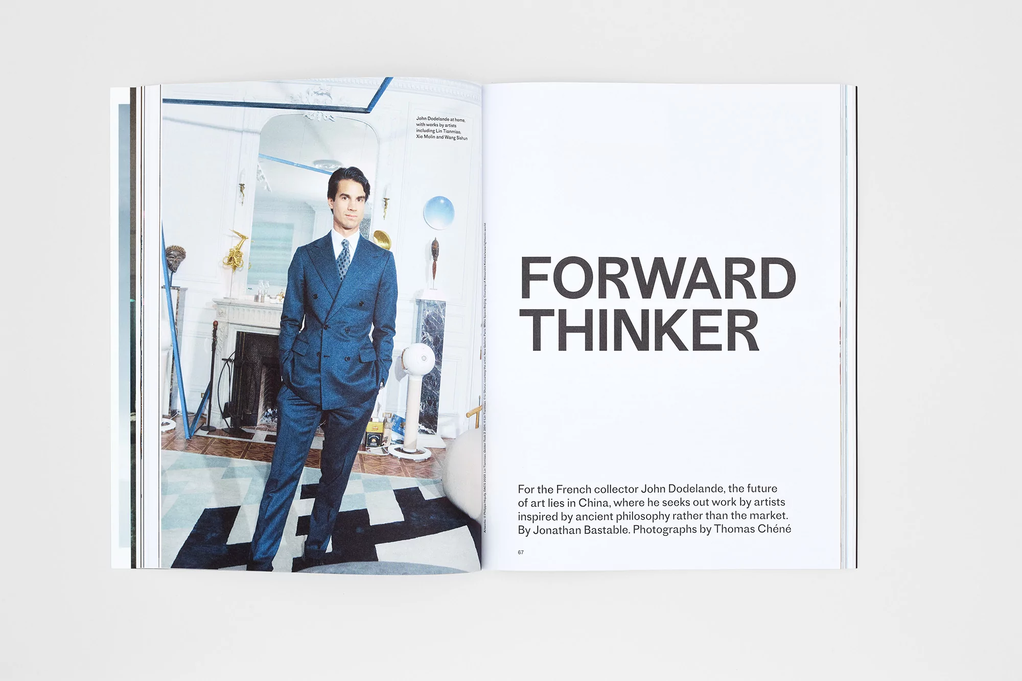 Fashion editorial shot of a man in a suit standing in a home interior with patterned floors and a large mirror, featured in a magazine spread.