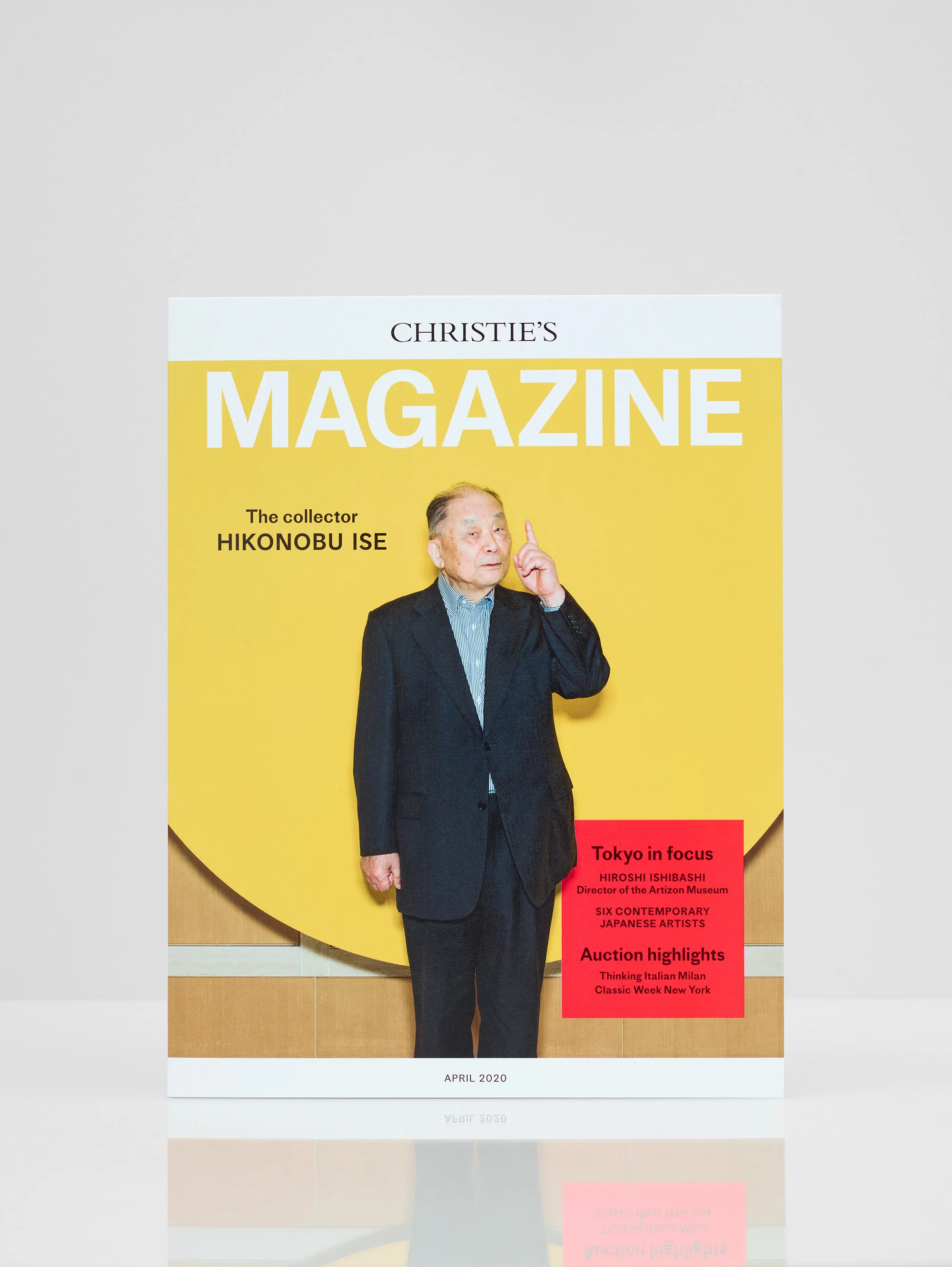 Christie's Magazine cover featuring a portrait of an older Asian man in a dark suit, pointing upwards, set against a yellow background.