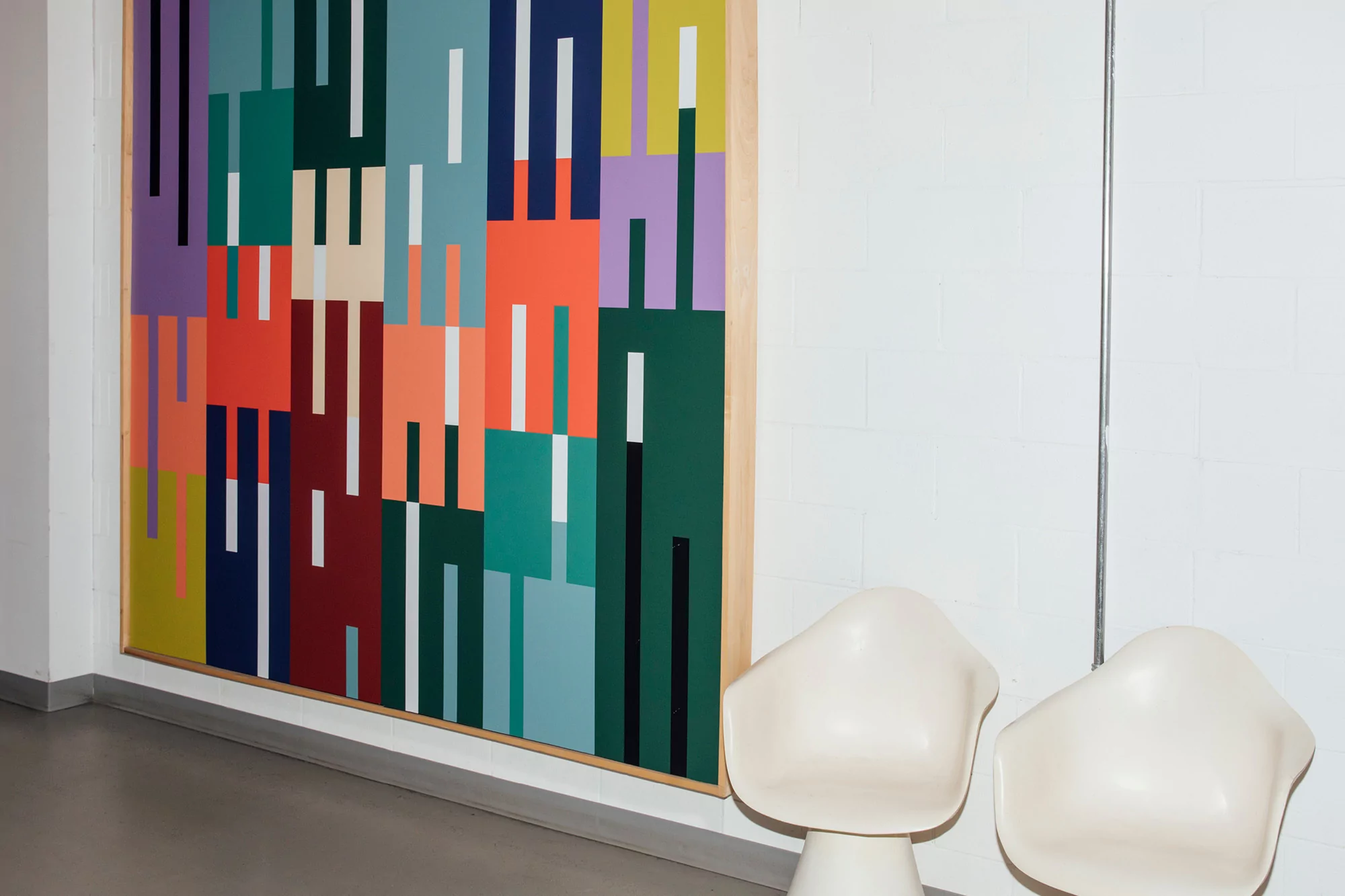Abstract geometric art with rectangles of vibrant colors including red, green, and purple, hangs on a white wall with two white chairs.