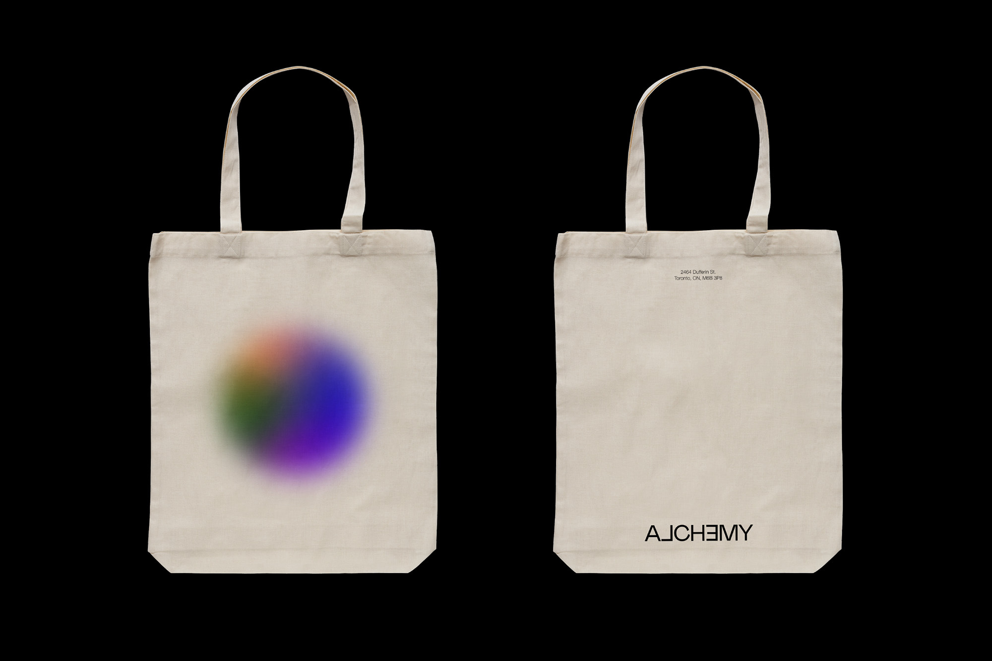 Two identical off-white canvas tote bags are isolated on black. The bag on the left has a blurred, rainbow-colored circle on it.
