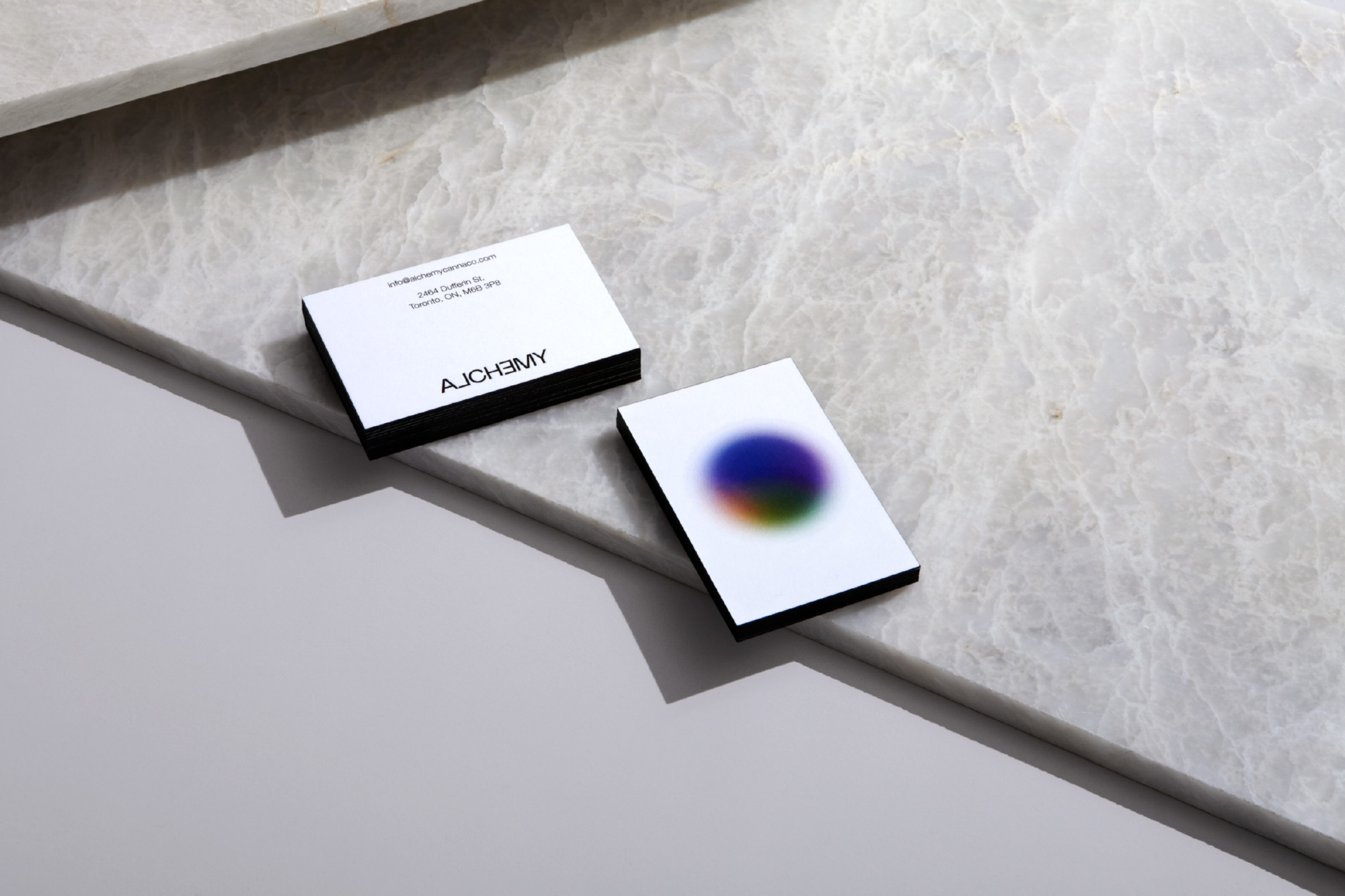 Two business cards angled on a marble surface. One card has a blurred colorful circle. Both are dark-edged with company name visible.
