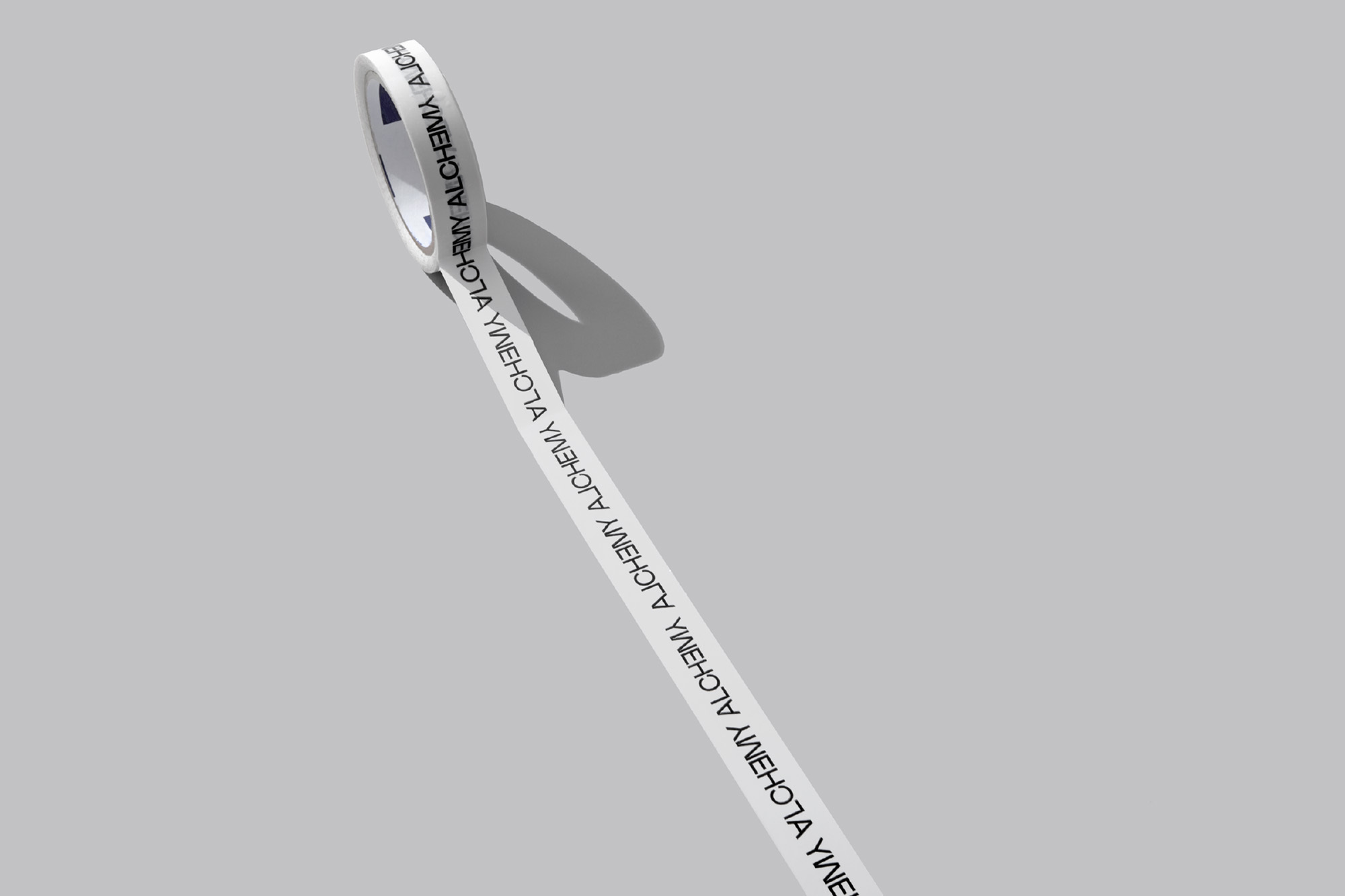Close-up of a roll of white tape with the word 'ALCHEMY' printed in black in a repeating pattern on a gray background.