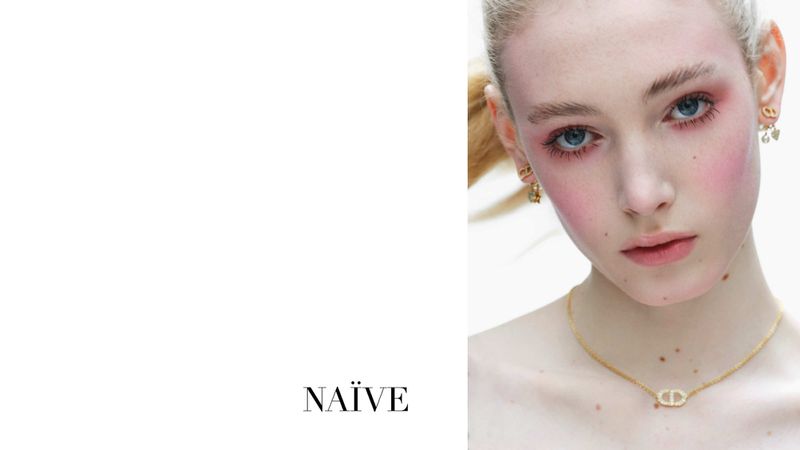 Close-up shot of a blonde woman wearing gold jewelry, with pink eye shadow and blush, against a white backdrop. The 'Naïve' logo appears.