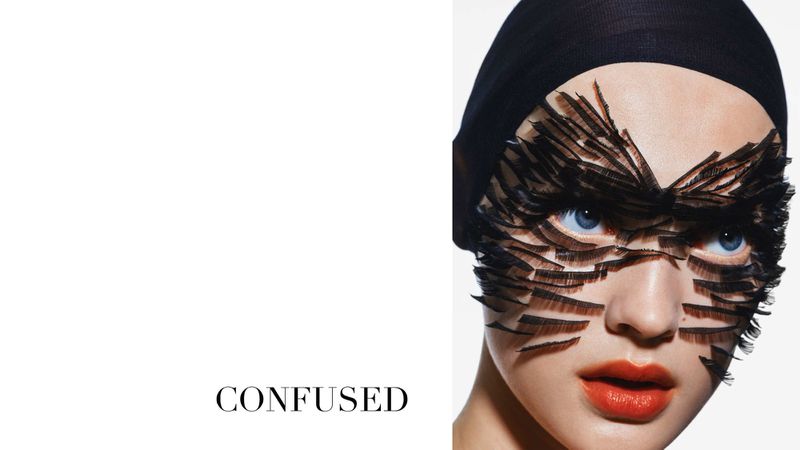 Close-up portrait of a woman with creative eyelash makeup and a black head covering against a bright white background; beauty shot.
