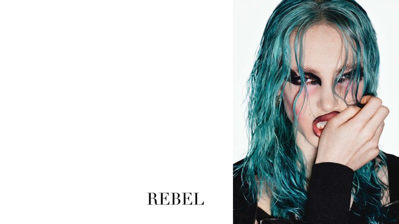 Close-up portrait of a model with teal wet-look hair and heavy black eye makeup, set against a stark white background with 'REBEL' text.