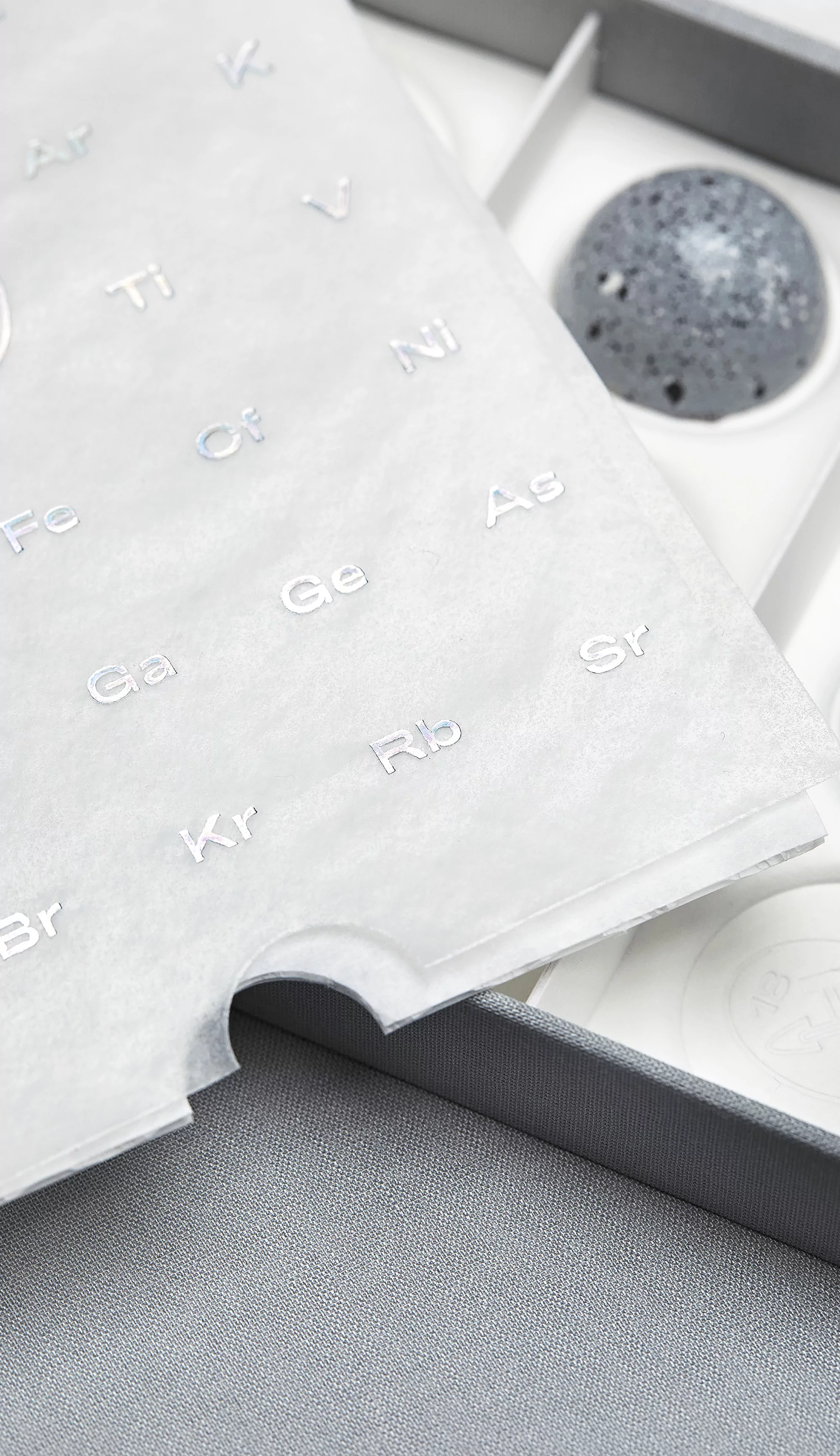 Grey box with chocolate bonbons decorated with a stone-like design and a paper with periodic table elements, elegant confectionary.