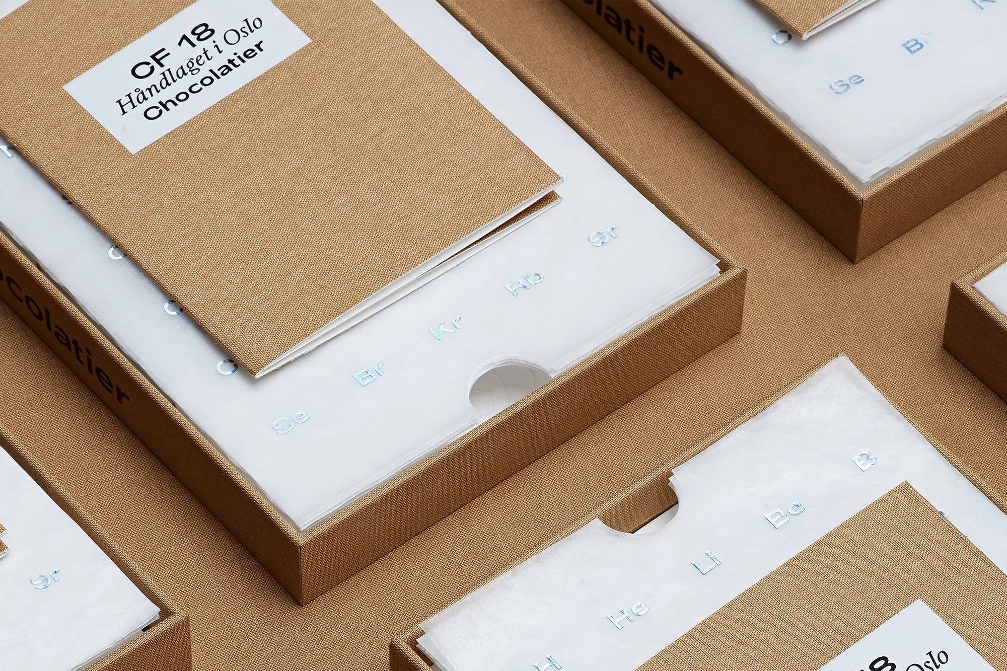Close-up of multiple tan-colored boxes with white inserts featuring repeating chemical element icons and text on the product packaging.