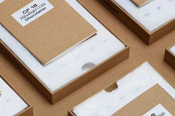 Close-up of multiple tan-colored boxes with white inserts featuring repeating chemical element icons and text on the product packaging.
