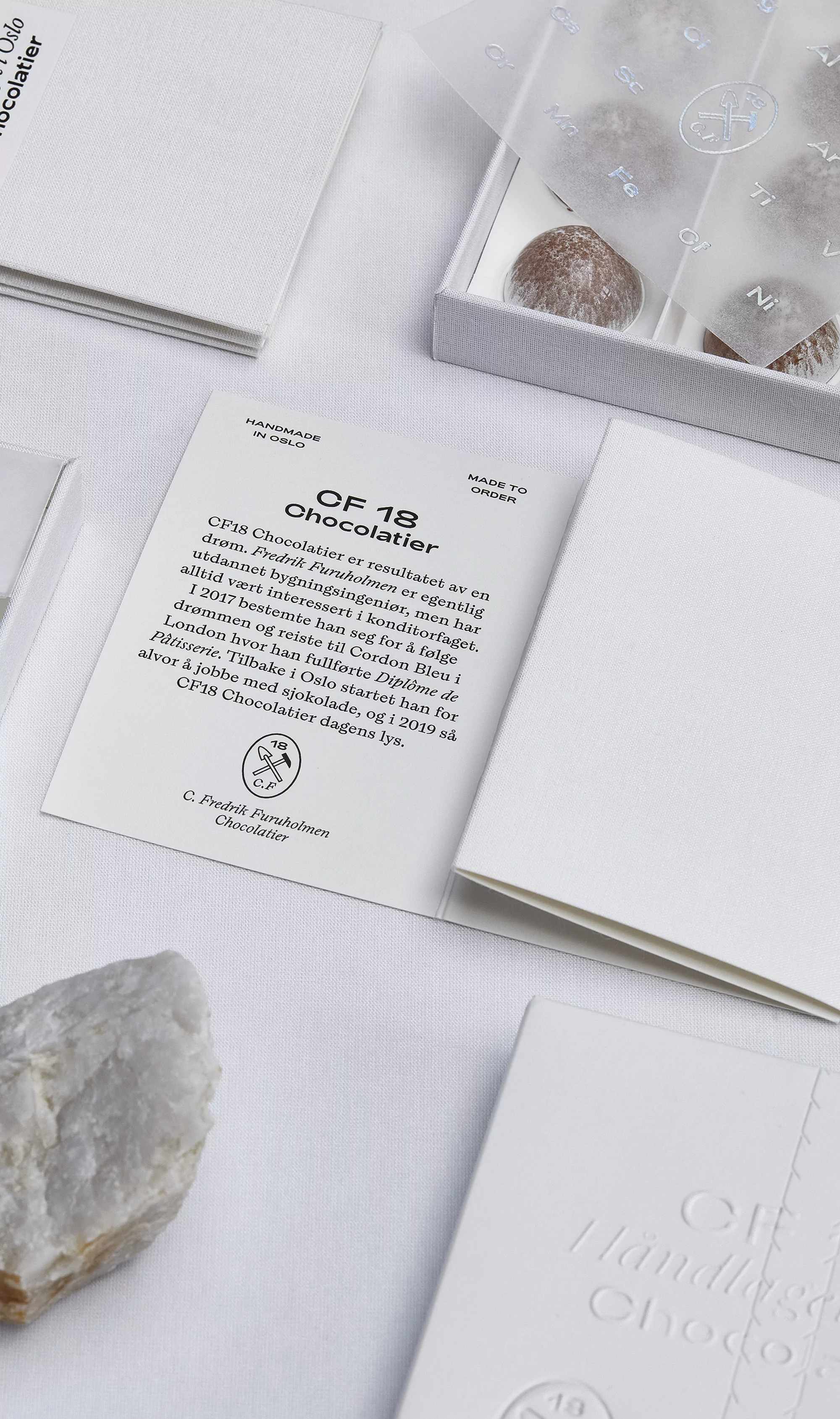 Close-up of CF18 Chocolatier handmade chocolates in a box with product literature, presented on a white surface.