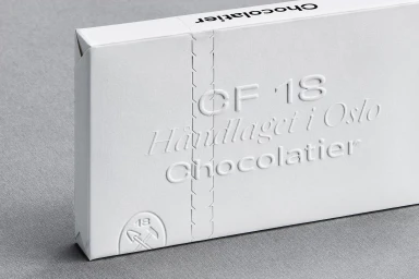 White embossed CF18 Chocolatier packaging resting on a textured grey surface