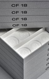 Stacked grey textured packaging boxes with CF 18 branding and white interior trays holding embossed circular chocolates