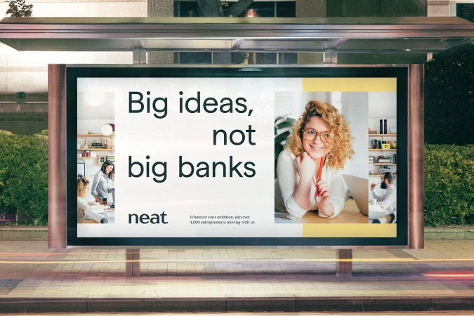 Billboard advertisement at night featuring a woman smiling, along with images of office work and the text: Big ideas, not big banks.