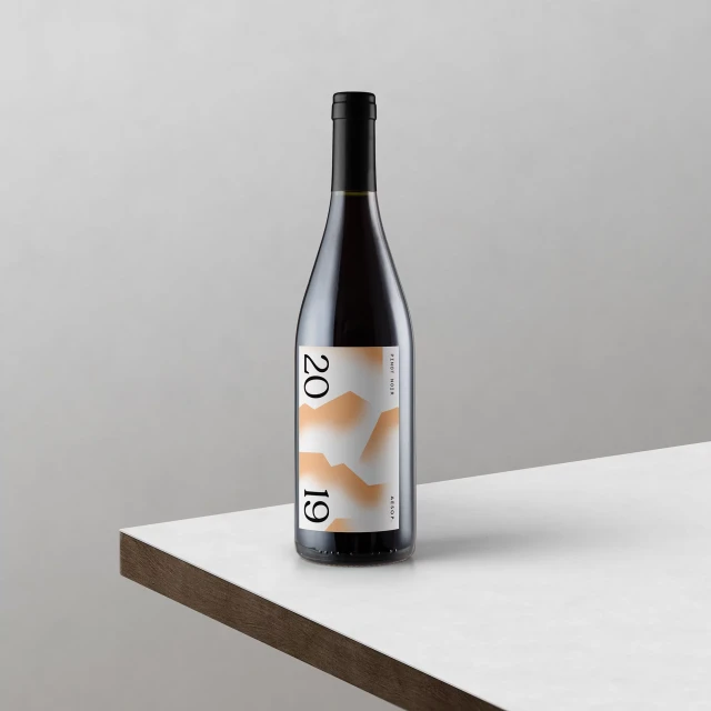 Studio shot of a dark wine bottle with peach mountain graphic on a white table against a neutral background for the food & beverage industry.
