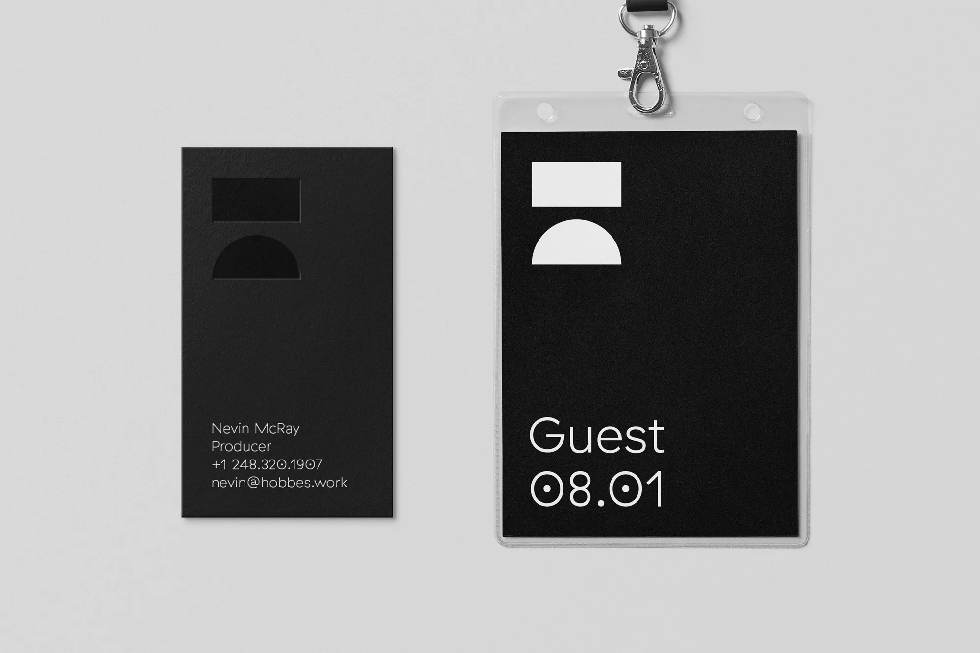 A black business card and a black guest pass in a clear plastic holder hanging from a lanyard, displayed against a light gray background.