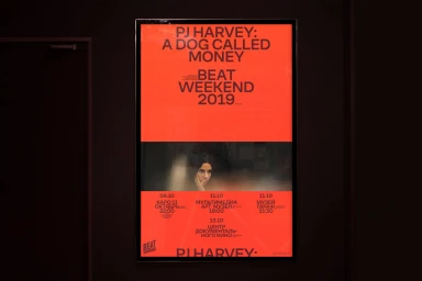 A vertically-oriented promotional film poster featuring bold black typography on a vivid red background displayed on a dark wall.