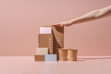 A hand resting on a stack of branded cardboard boxes and paper cups against a pink background