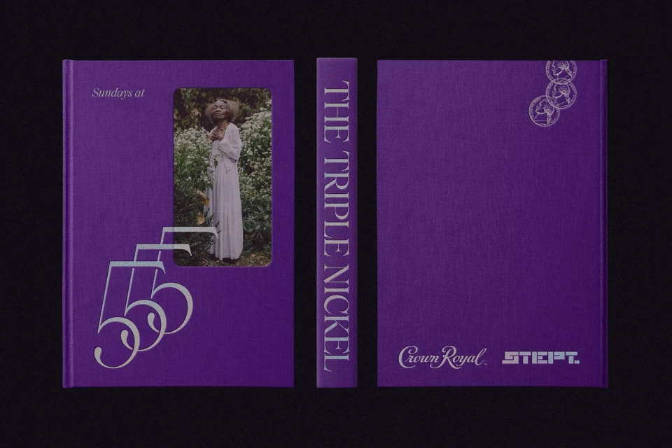 Studio shot of a closed purple book with a photograph of a woman in nature, stacked on a black surface with a black background.