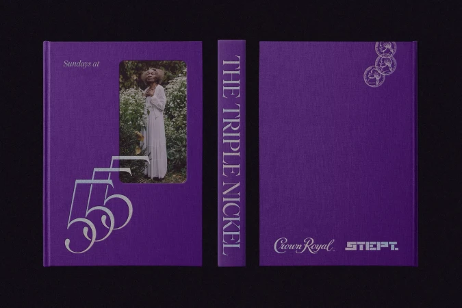 Studio shot of a closed purple book with a photograph of a woman in nature, stacked on a black surface with a black background.