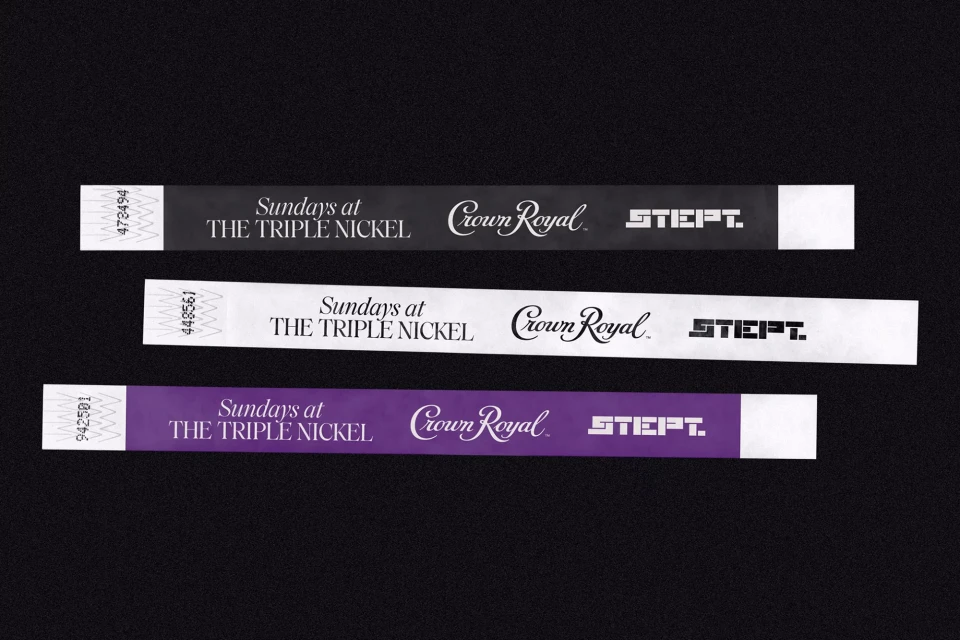 Three wristbands in black, white, and purple, each printed with event details and branding, displayed against a dark background.
