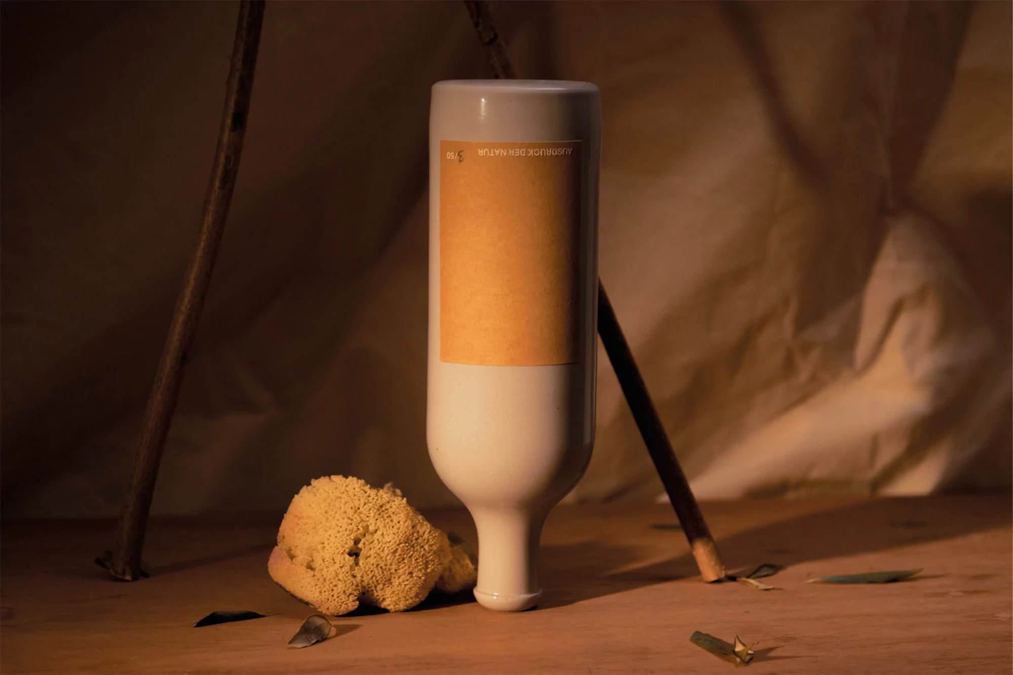 Minimalist product shot of a cream-colored bottle with a yellow label next to a natural sponge on a wood surface against a tan background.