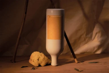 An inverted white ceramic bottle with a yellow label resting upside down on a wooden surface beside a natural sea sponge.