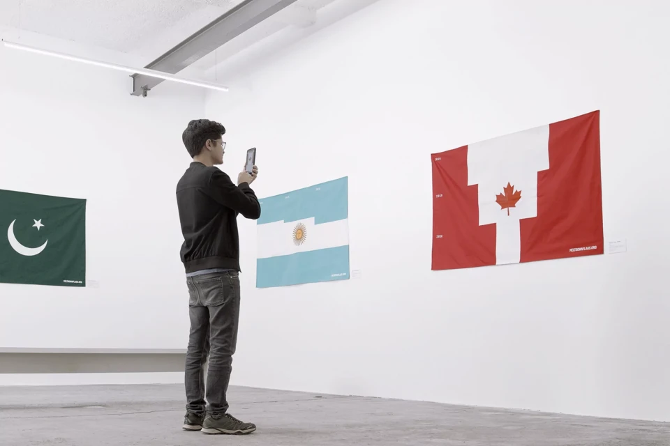 Person photographing flags of Canada, Argentina and Pakistan in an art gallery. Bright white walls and concrete floor. 