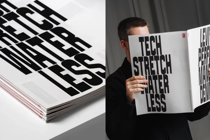 Adult man reading a black-and-white magazine with bold text, set against a neutral background. Magazine stack visible on a white surface.