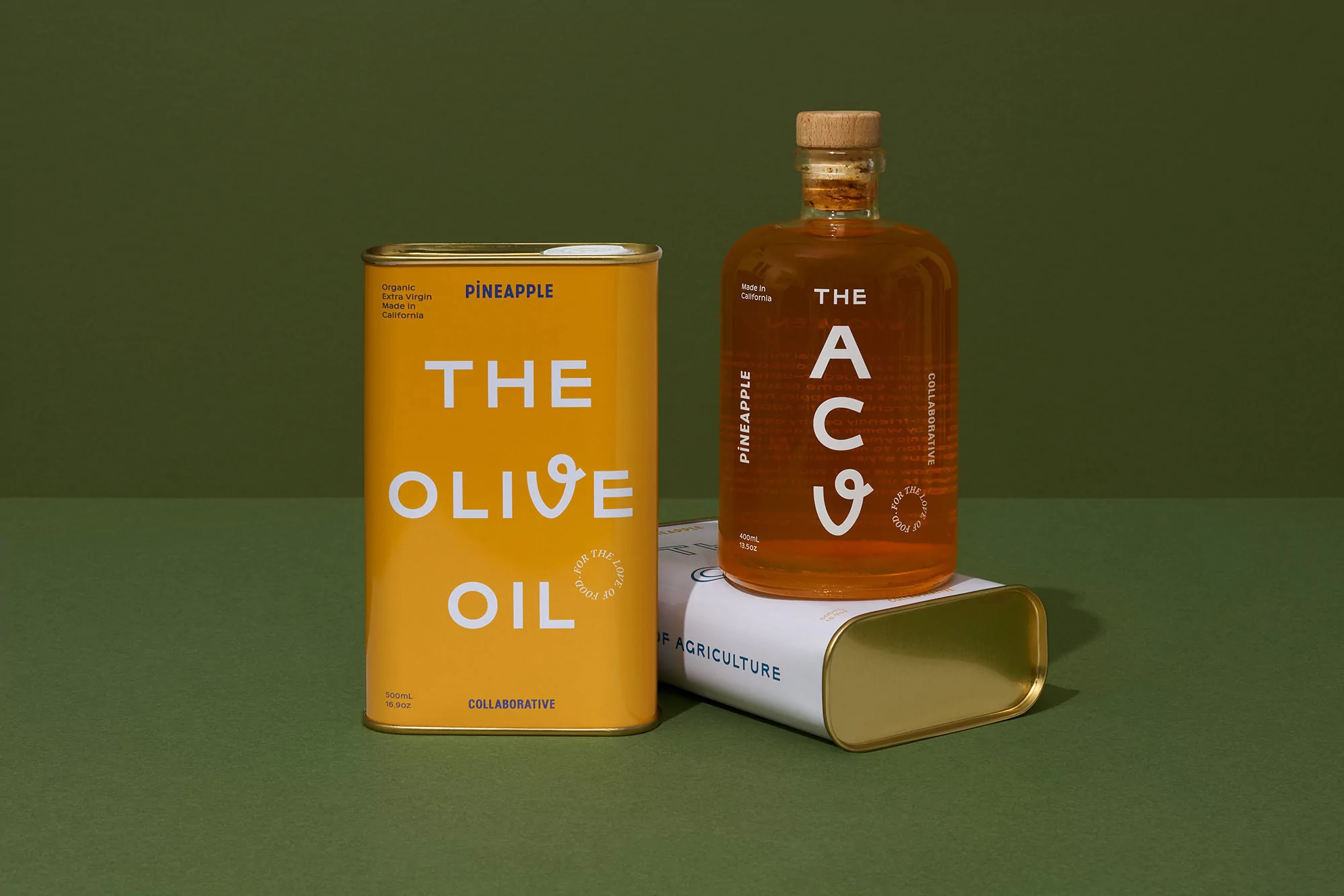 Still life shot of a yellow olive oil tin and a glass bottle filled with olive oil against a green background in a studio setting.
